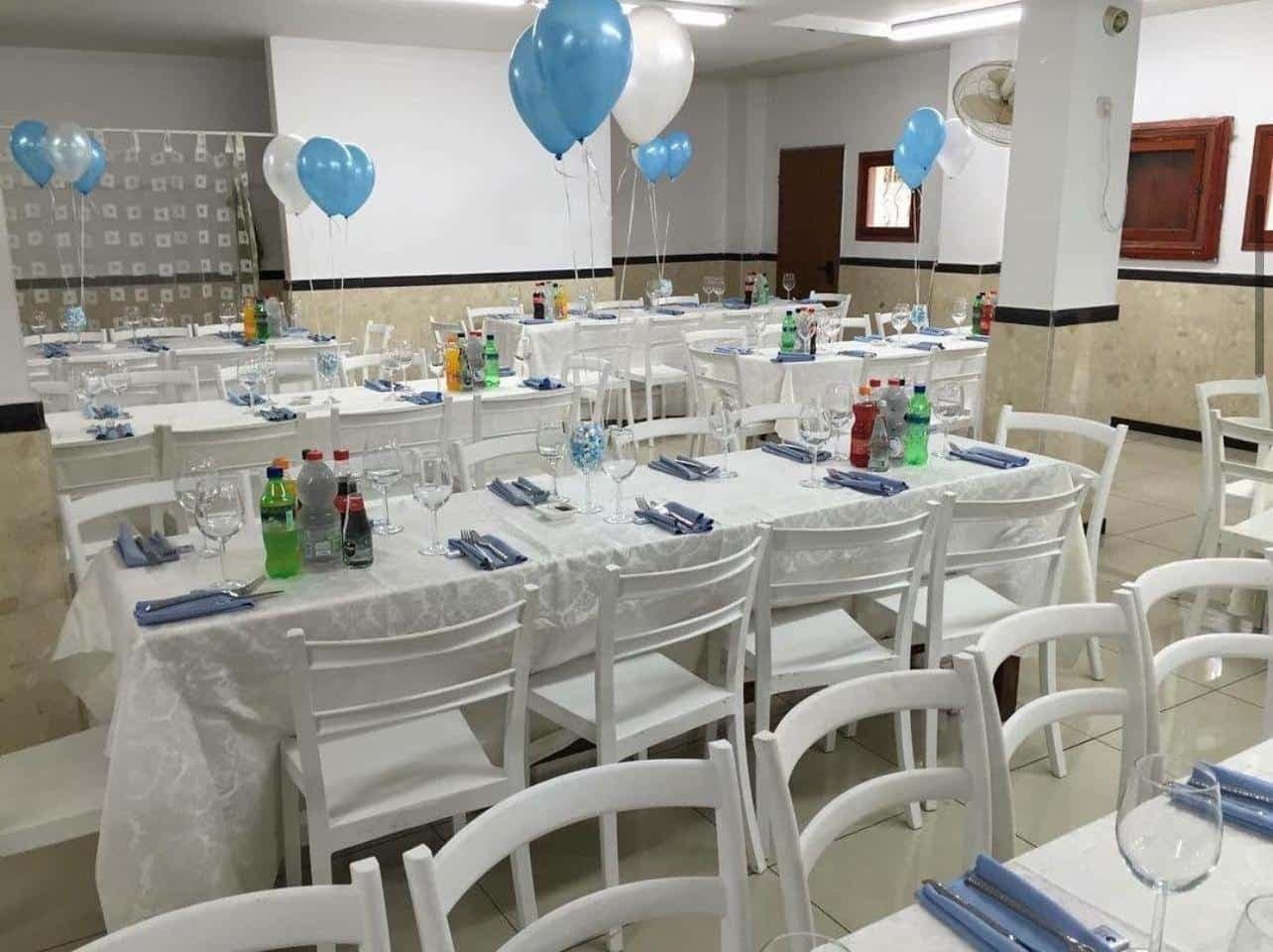 שולחנות מעוצבים לאירועים עם כסאות לבנים, בלונים כחולים ומשקאות ממותגים. השכרת ציוד לאירועים.